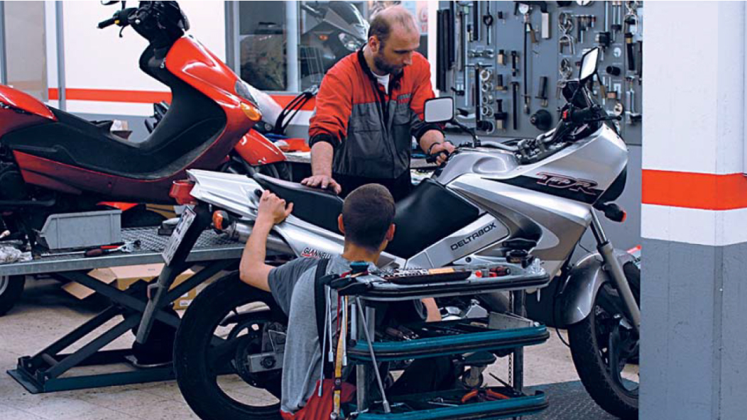 Foto van een werkplaats waar twee mensen aan een motorfiets werken.