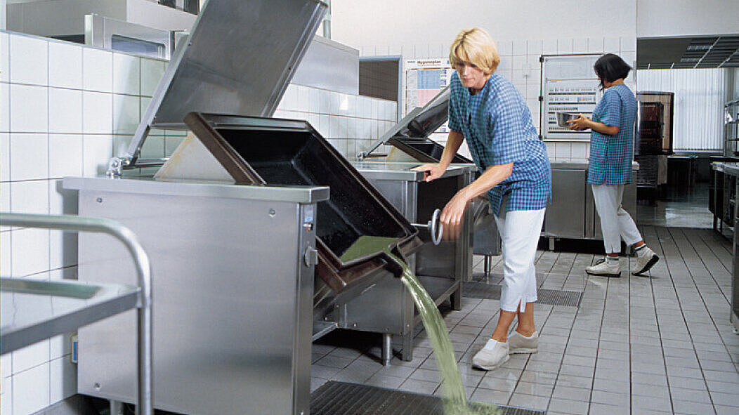 In een grootkeuken wordt een grote kookpan in een vloerbak geleegd.
